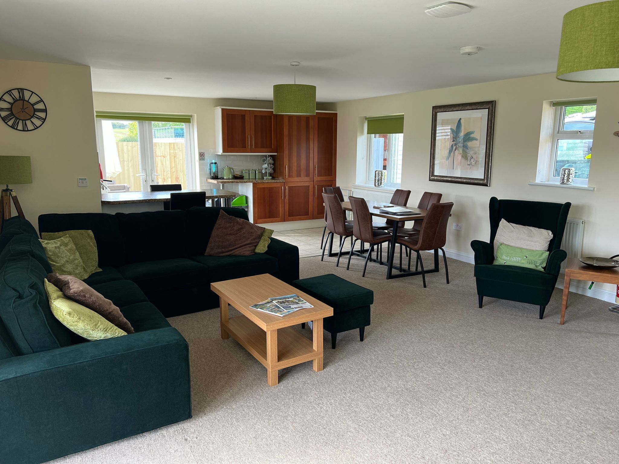 Een woonkamer met een groene bank, een houten salontafel, en een eethoek met een tafel en stoelen.