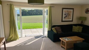Een woonkamer met een donkergroene bank, een houten salontafel en uitzicht op een groen veld door glazen deuren.