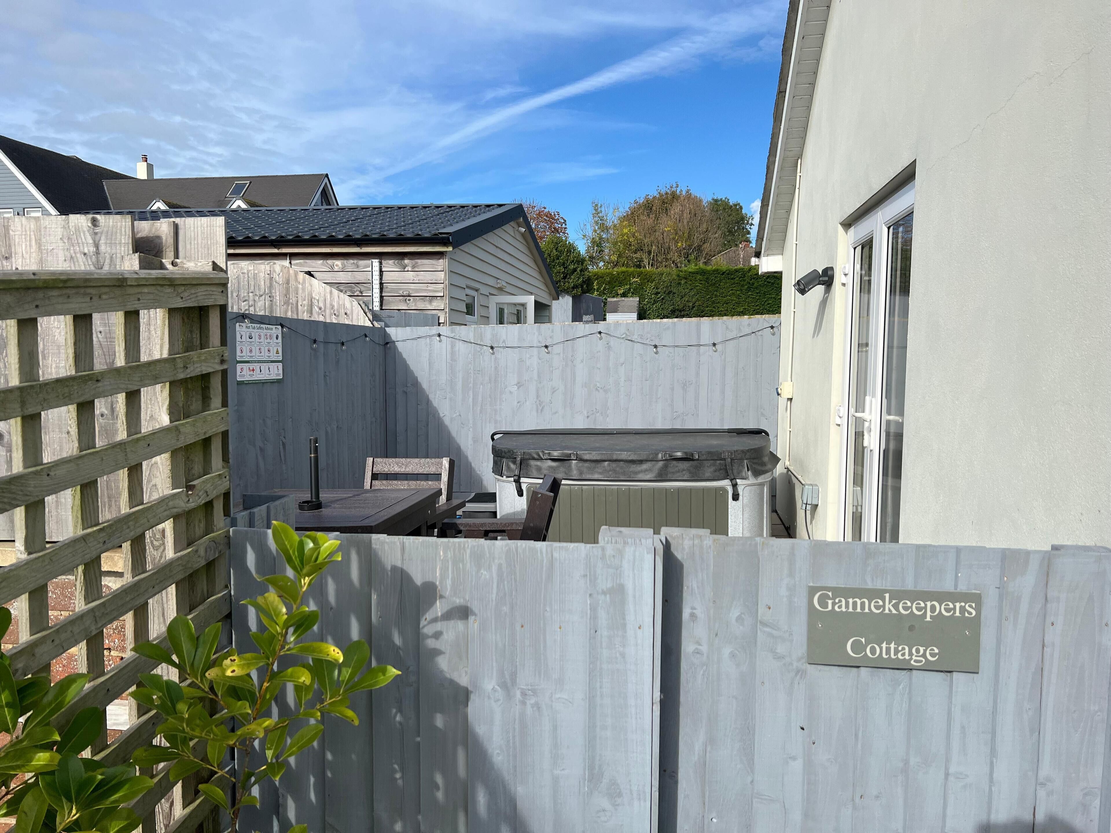 Ein umzäunter Garten mit Whirlpool, Holztisch und Stühlen. Ein Schild zeigt 
