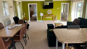 Een moderne woonkamer met een eethoek, een aan de muur bevestigde televisie en een bed op de achtergrond.