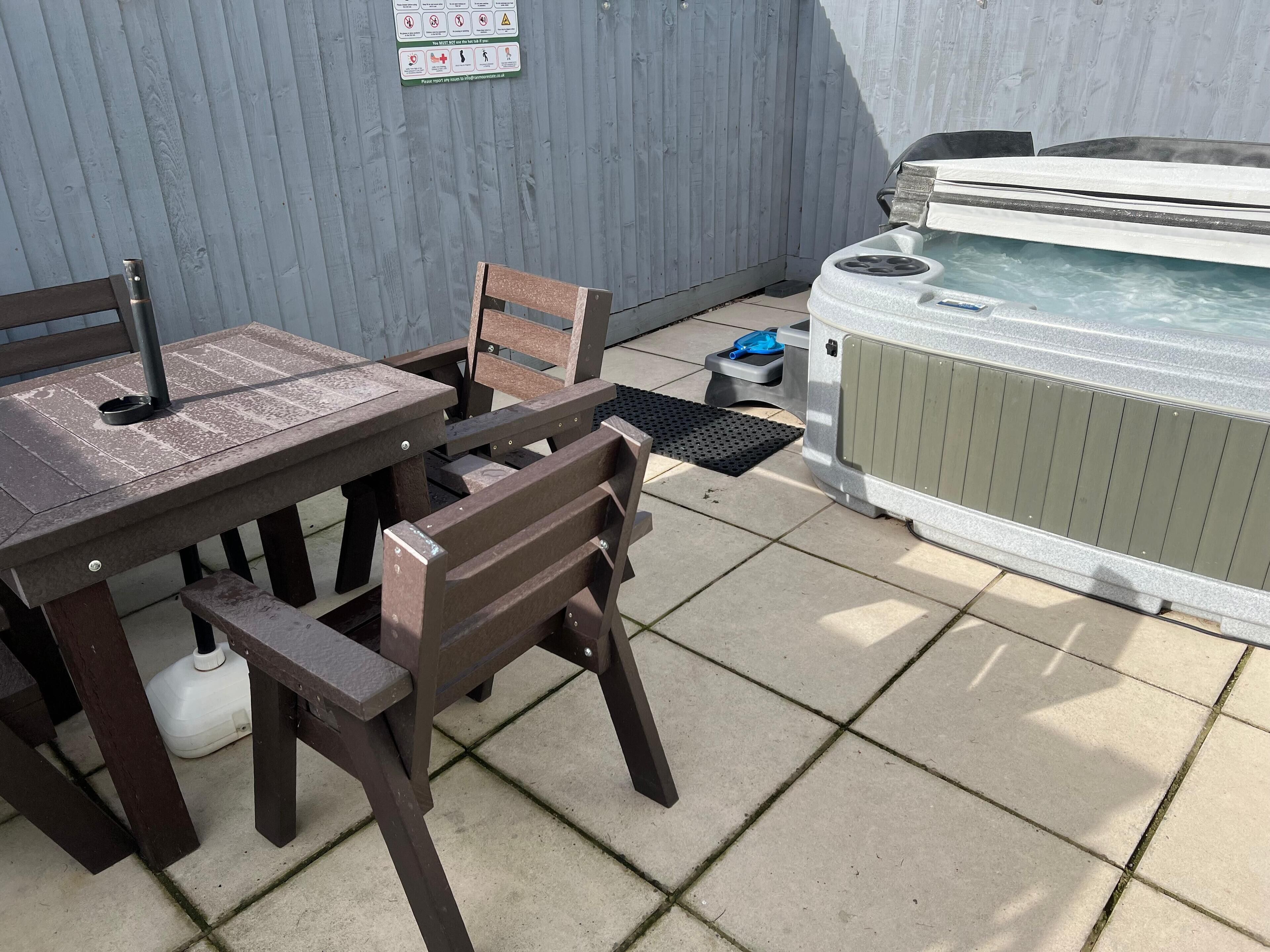 Un patio al aire libre con mesa y sillas de madera, un jacuzzi y suelo de baldosas.