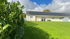 Een gebouw met een dakbedekt met zonnepanelen, een verzorgd gazon en een bank.