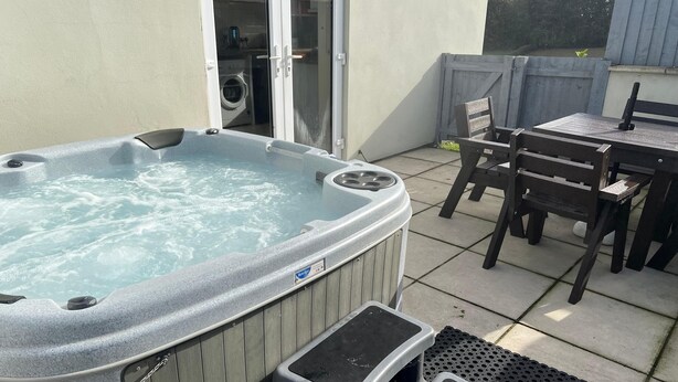 Een hottub met een houten buitenkant, een tafeltje en stoelen, en een overdekte zithoek.