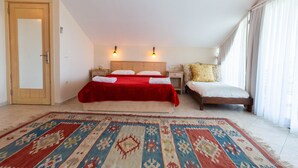 A bedroom with a large bed, a smaller bed, a patterned rug, and a wooden door. - 4-Bedroom Cappadocia Stone Villa in Charming Gökbel with Pool & Scenic Views (Gökbel)