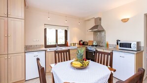 A compact kitchen with wooden cabinets, a dining table with a fruit bowl, and modern appliances. - 4-Bedroom Cappadocia Stone Villa in Charming Gökbel with Pool & Scenic Views (Gökbel)