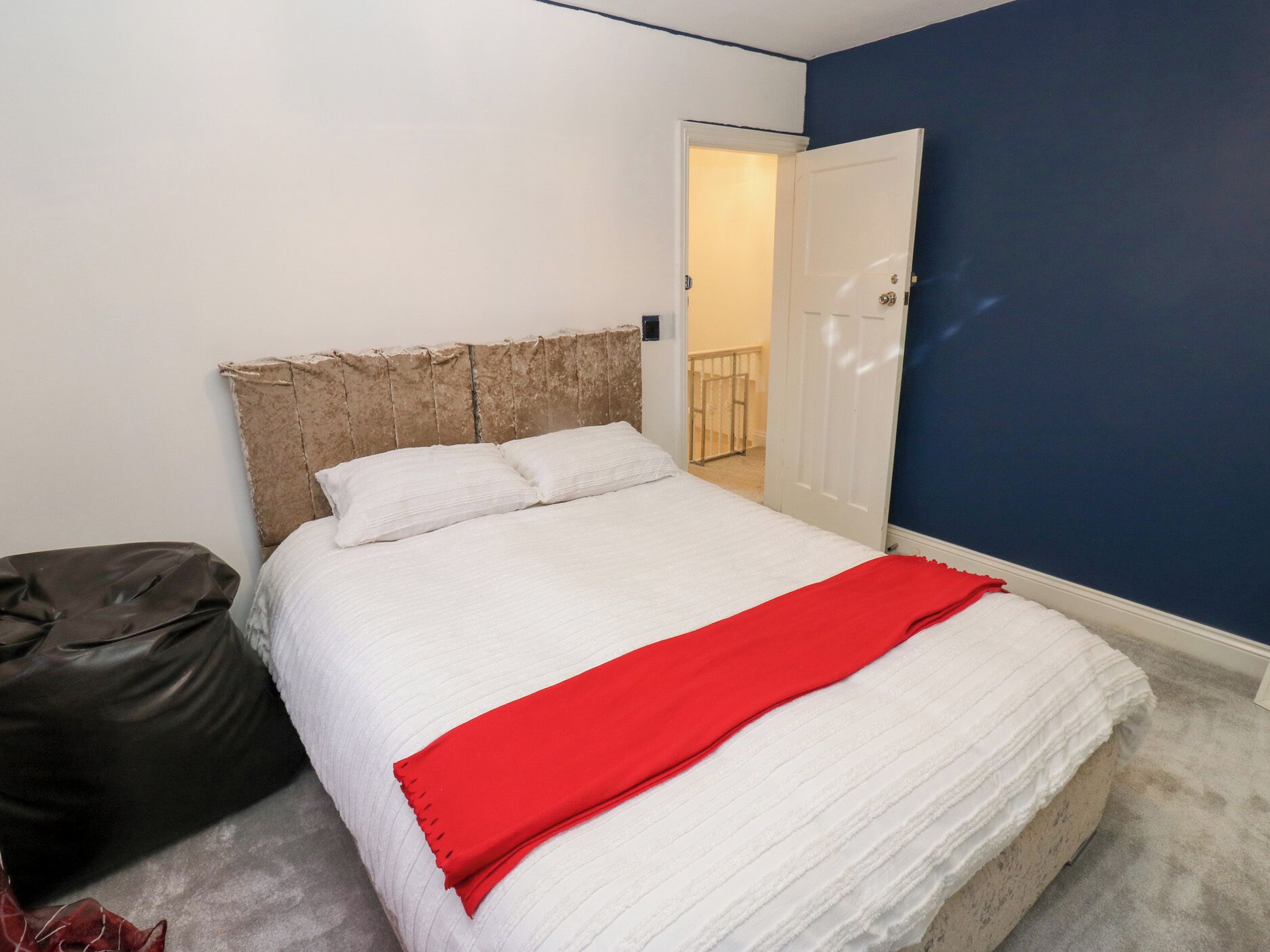 Ein Schlafzimmer mit einem Bett, einer roten Decke, einem weißen Kopfteil und einer Tür, die auf einen Balkon führt.