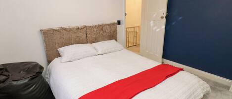 Ein Schlafzimmer mit einem Bett, einer roten Decke, einem weißen Kopfteil und einer Tür, die auf einen Balkon führt.