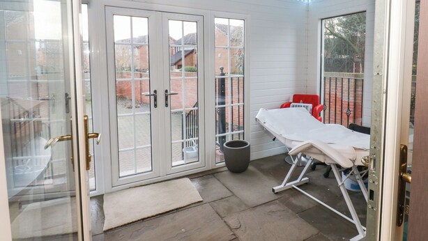 A room with a sliding glass door, a small table with a white tablecloth, and a red chair. - Middleton Park House (Leeds)
