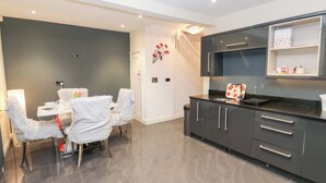 A modern kitchen with dark cabinets, a countertop, and a dining area with a table and chairs. - Middleton Park House (Leeds)