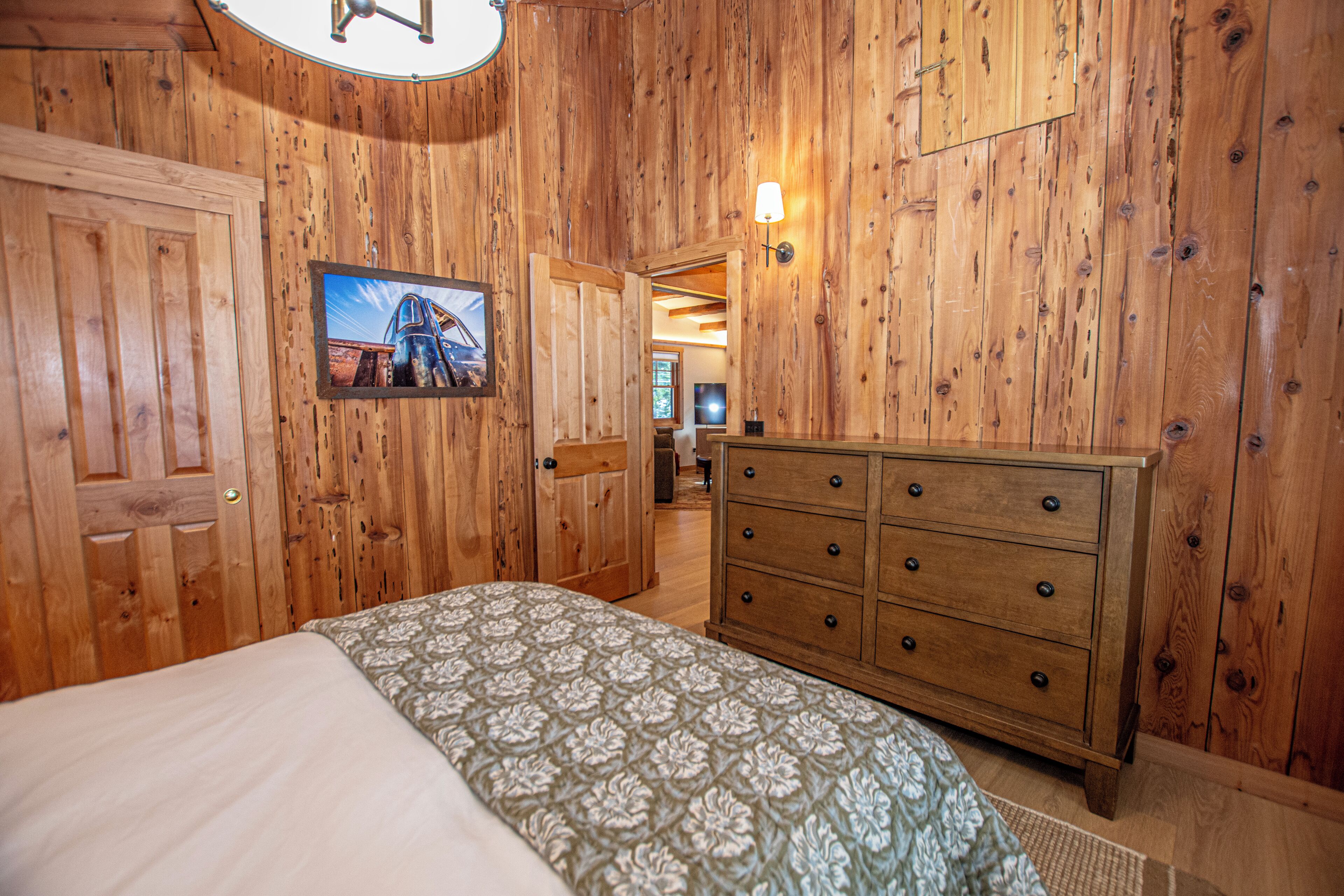 Ein Zimmer mit Holzwänden, einem Bett, einer Kommode und einem gerahmten Bild an der Wand.