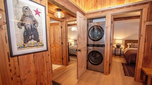 A wooden interior with a laundry area, a framed artwork, and a bed with a patterned headboard. - Cedar Cottage by Hauserman Rentals (Homewood)