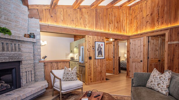 A cozy living room with a fireplace, wooden walls, a sofa, and a dining area. - Cedar Cottage by Hauserman Rentals (Homewood)