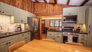 A kitchen with wooden beams, white cabinets, a wooden dining table, and a built-in oven. - Cedar Cottage by Hauserman Rentals (Homewood)
