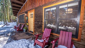 A wooden cabin with a porch, large windows, and red Adirondack chairs with snow on them. - Cedar Cottage by Hauserman Rentals (Homewood)