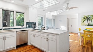 A modern kitchen with white cabinetry, a dishwasher, and a large island. There is a dining area with a yellow table and chairs. - Stunning Sea Pines Retreat with private pool and spa (Hilton Head Island)