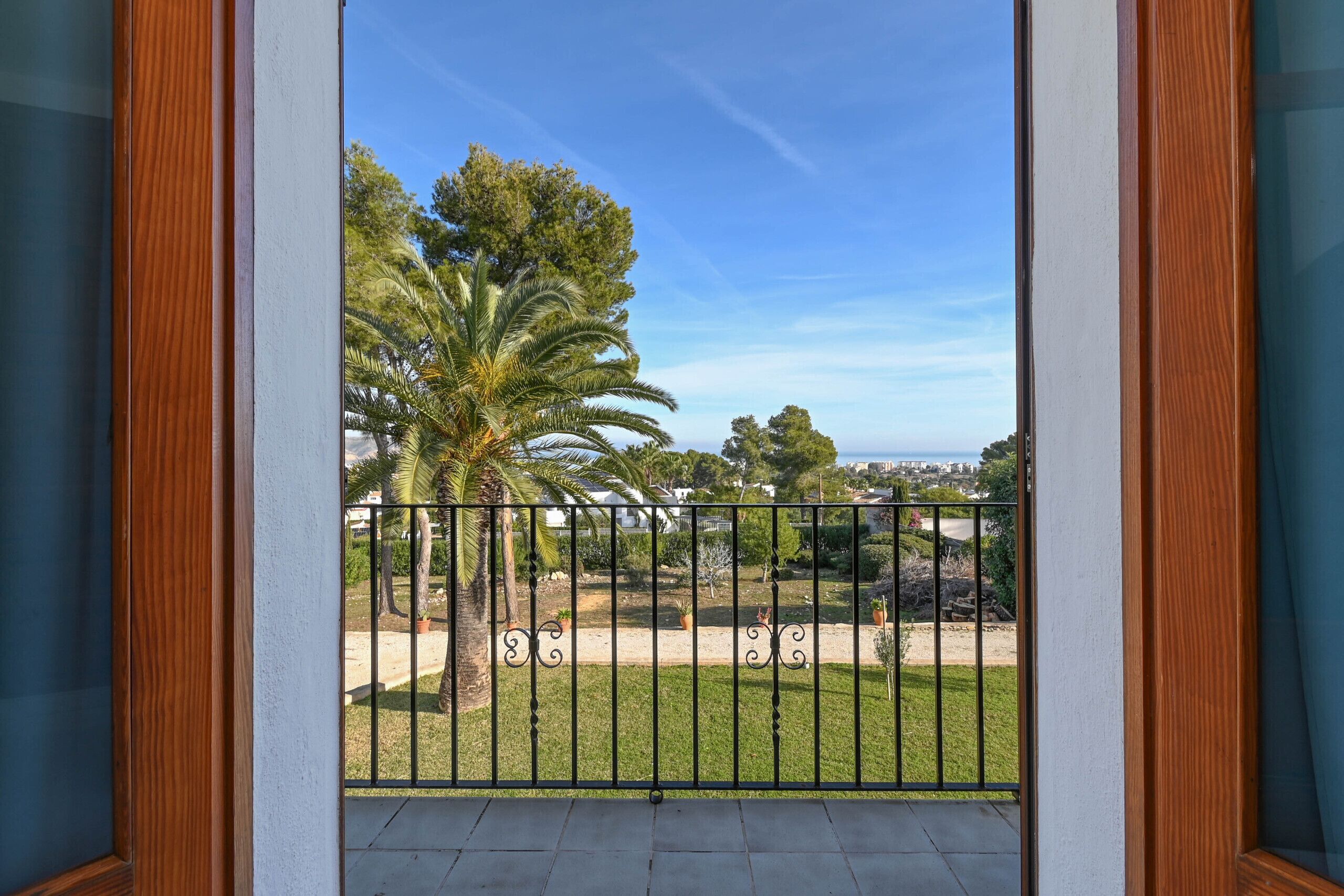 A balcony with a view of a landscaped garden, including palm trees and a fence.