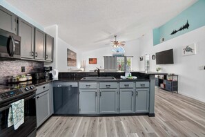 A modern kitchen with grey cabinets, a black countertop, and a central island. - Woodland Yards, Private Escape Close To Disney 3 Bedroom Home (Kissimmee)