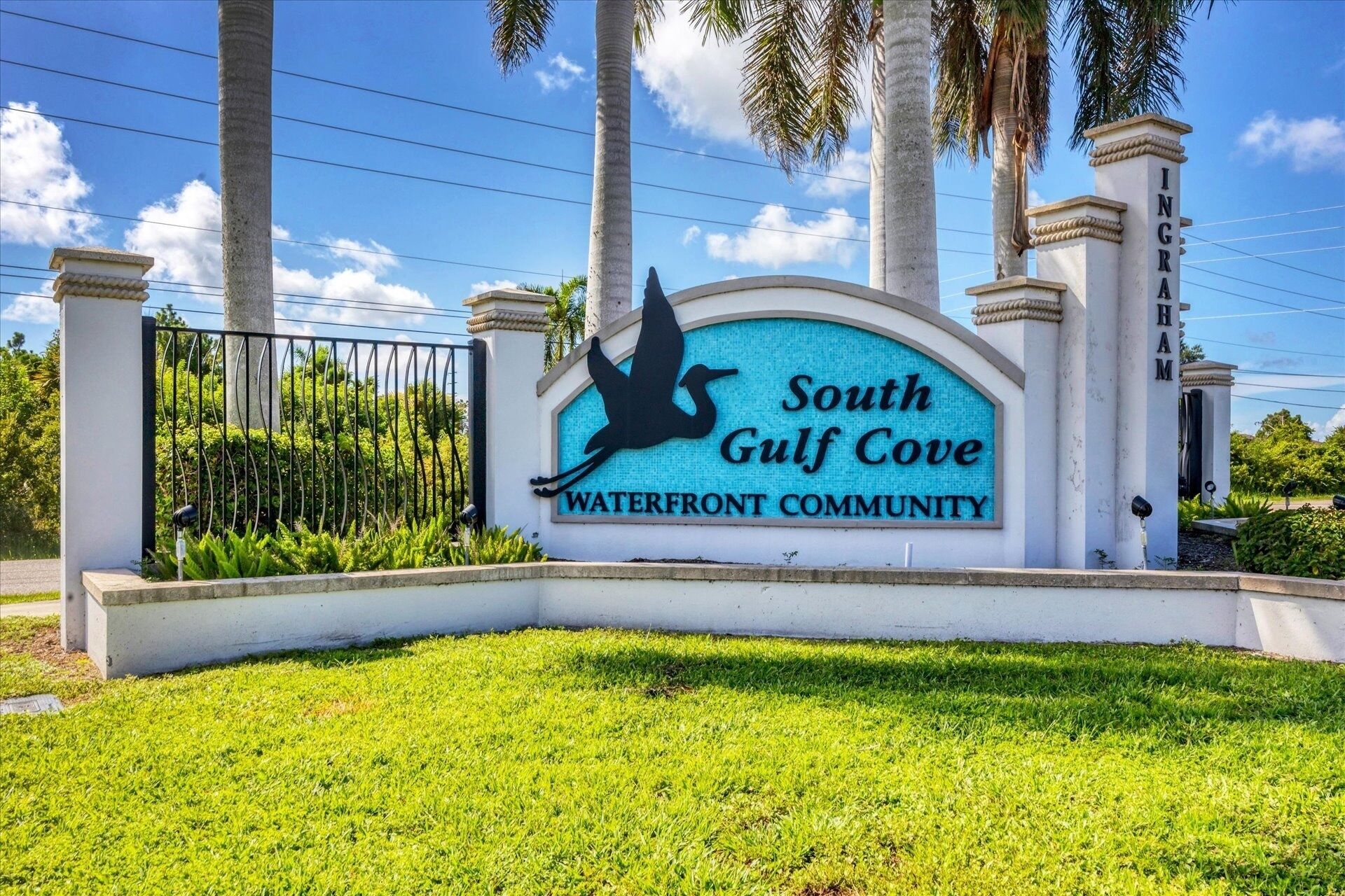 A sign for South Gulf Cove Waterfront Community with a bird silhouette, palm trees, and a clear sky.
