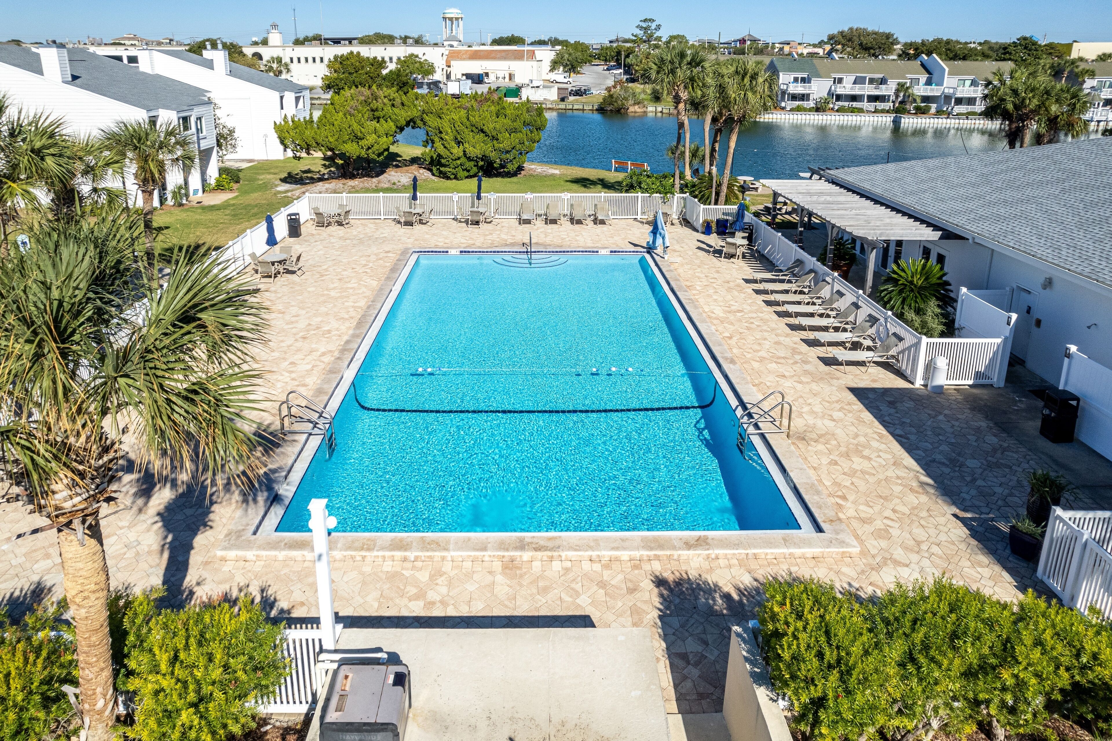 Ein rechteckiger Pool mit Fliesen umgeben, Palmen säumen die Umgebung und es bietet sich ein Blick auf ein Gewässer.