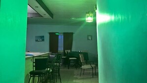 A room with a green-lit ceiling, a piano, and several chairs arranged for a small gathering. - NevaLand County Hotel (Matiliku)