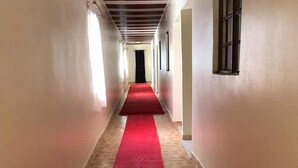 A long hallway with a red carpet, tiled floor, and white walls. - NevaLand County Hotel (Matiliku)