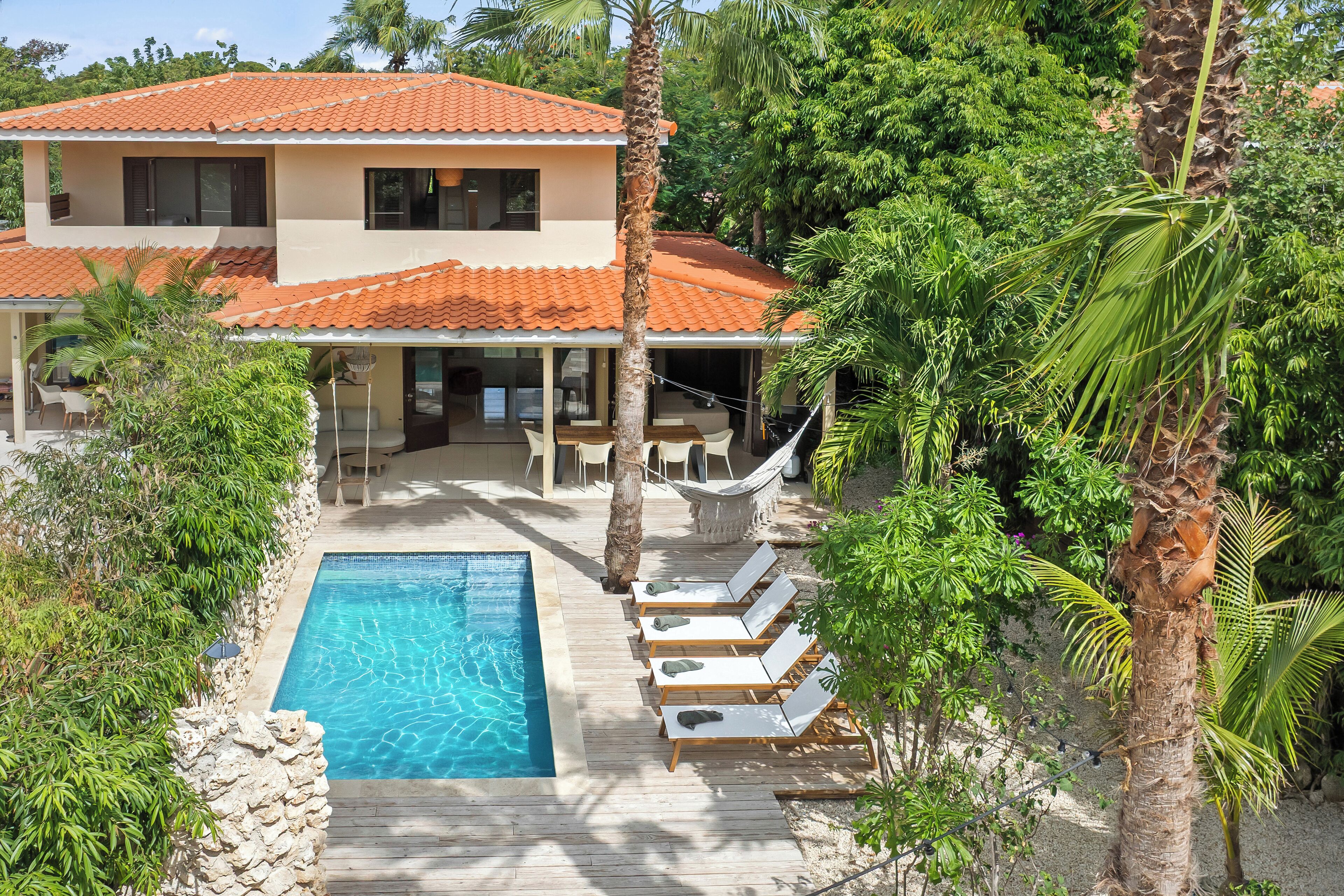 A two-story house with a swimming pool, lounge chairs, and a hammock.