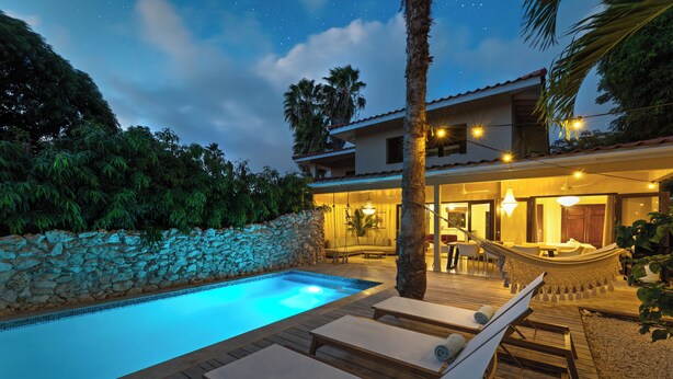 A pool area with lounge chairs, a stone wall, and a building with outdoor seating. - Villa The Hidden Palm, Piscadera, Private Pool (Willemstad)