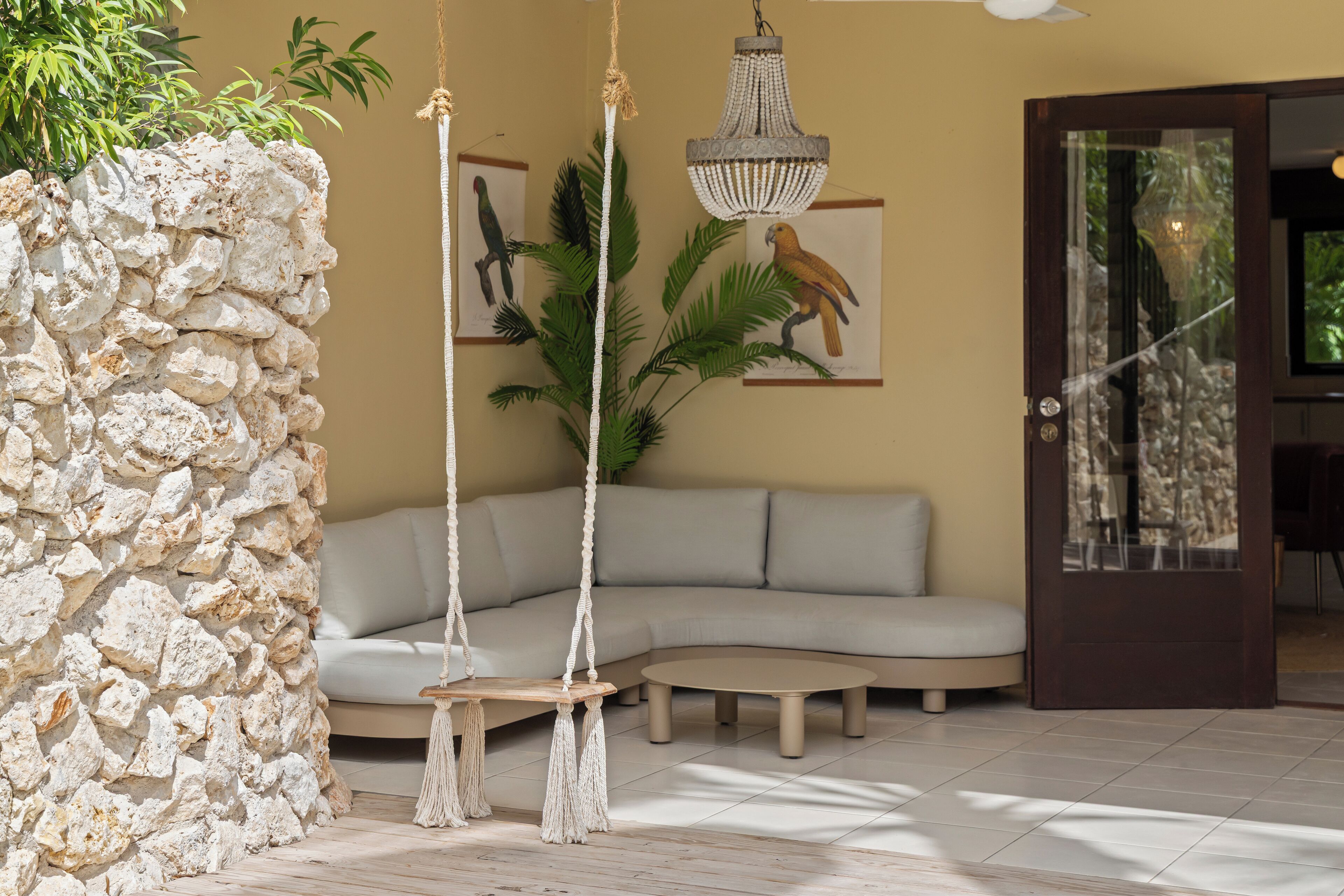 A modern living room with a stone wall, a grey sofa, a hanging chandelier, and a tropical plant.