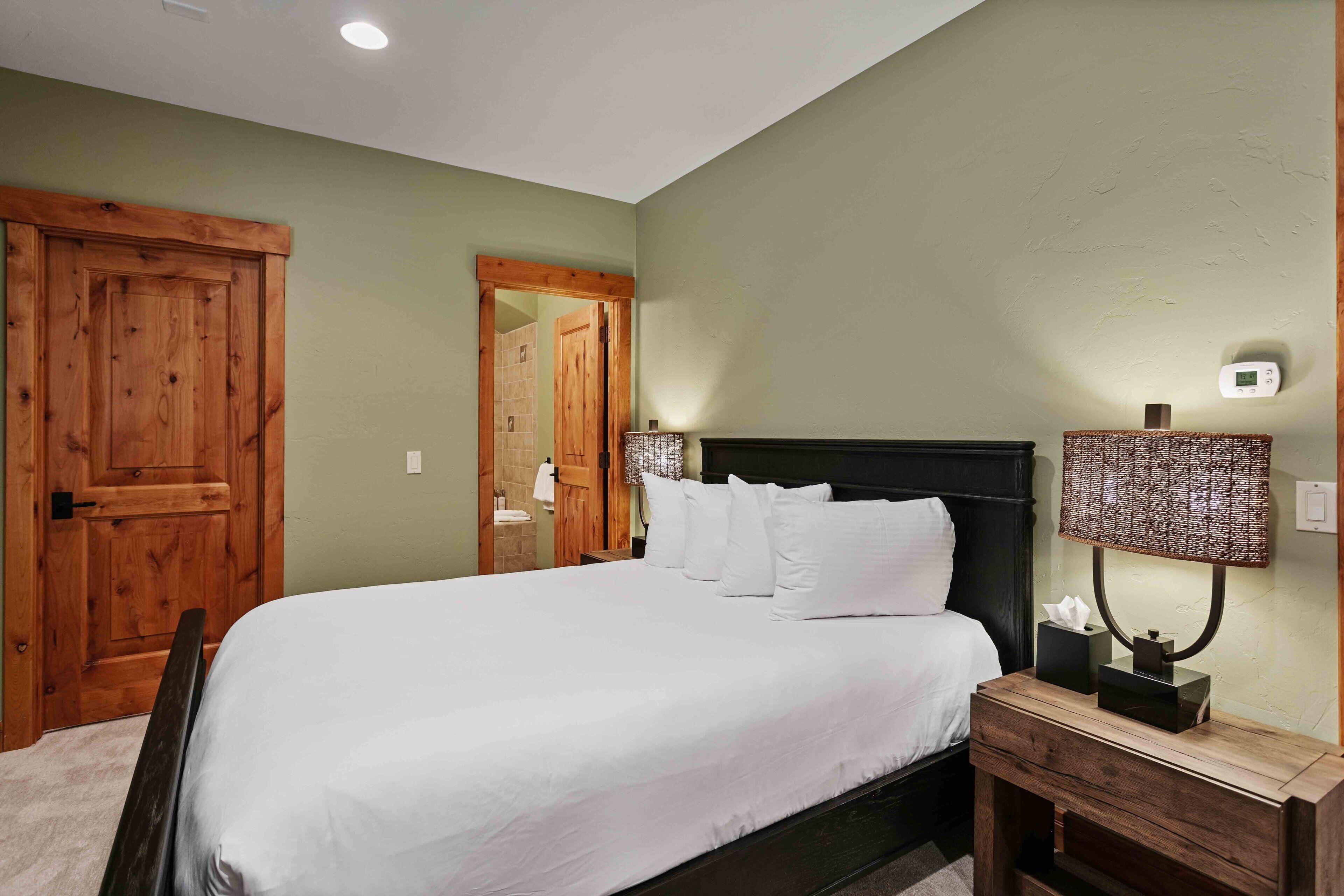 Un dormitorio con una cama grande, cabecera de madera, mesita de noche y una lámpara fijada a la pared.