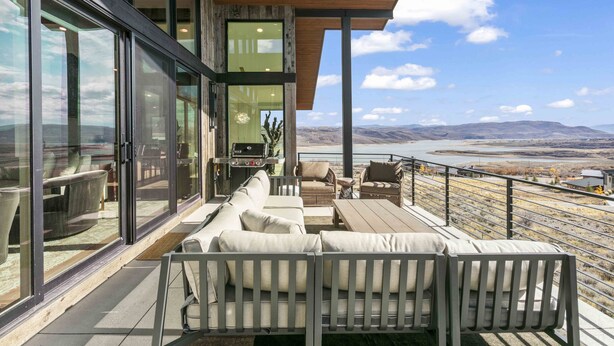 A modern outdoor living area with a sofa and chairs, a wooden deck, and a view of a river and mountains. - Luxury 4br W/ Hot Tub & Deer Valley Access 4 Bedroom Home (Heber City)
