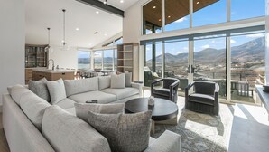 A spacious living area with a large sectional sofa, a round coffee table, and a view of mountains through large windows. - Luxury 4br W/ Hot Tub & Deer Valley Access 4 Bedroom Home (Heber City)
