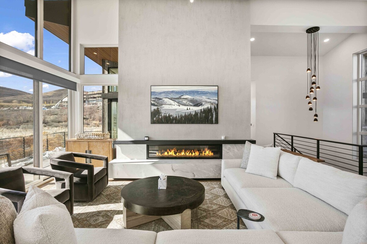 A modern living room with a fireplace, large windows, and a view of the outdoors.