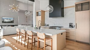 A modern kitchen with a large island, wooden bar stools, a built-in stove, and a large black range hood. - Luxury 4br W/ Hot Tub & Deer Valley Access 4 Bedroom Home (Heber City)