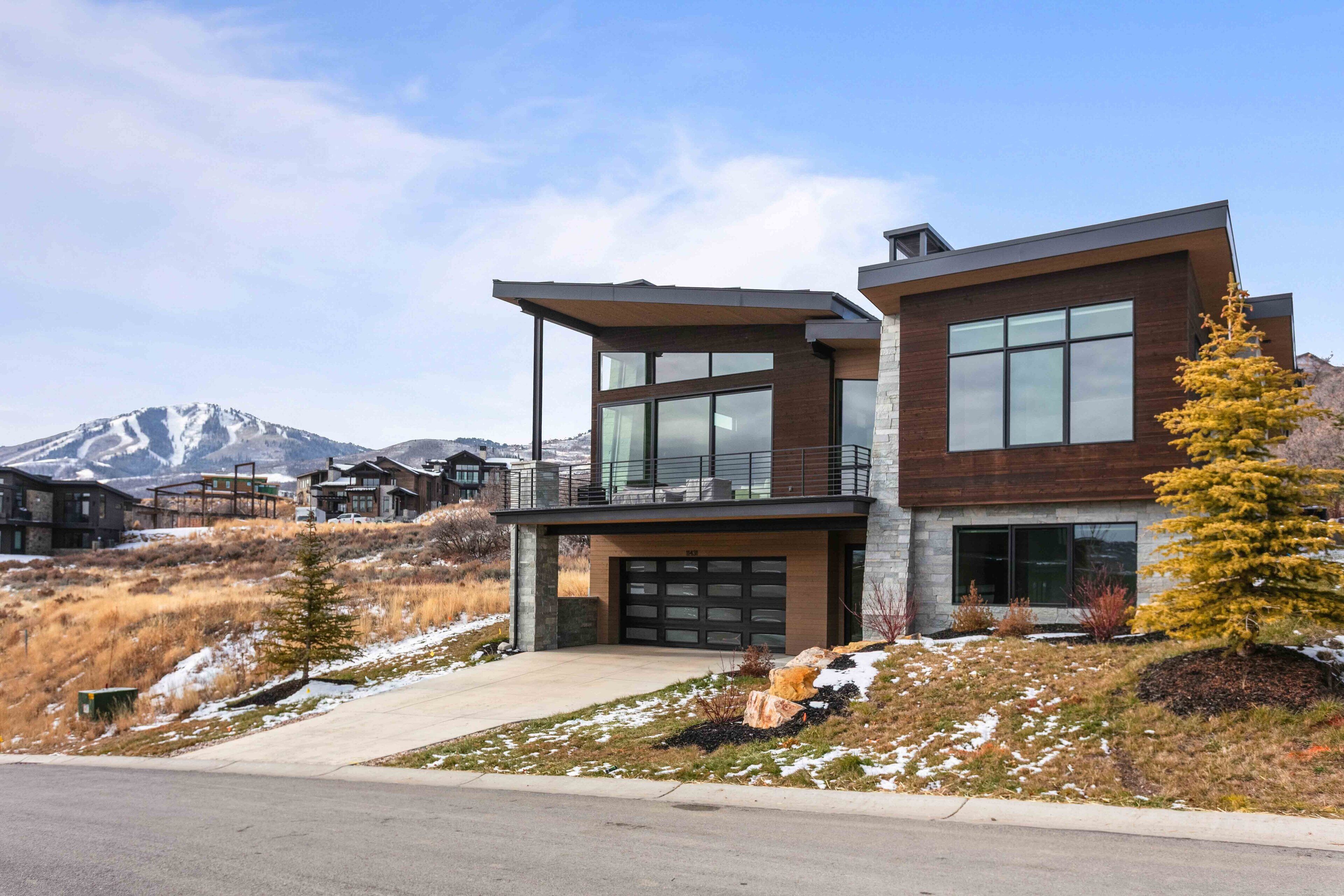A modern two-story house with large windows, a garage, and a mountain backdrop.