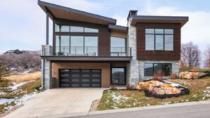 Une maison moderne à deux étages, dotée d’un grand garage, d’un balcon et d’une façade en pierre.
