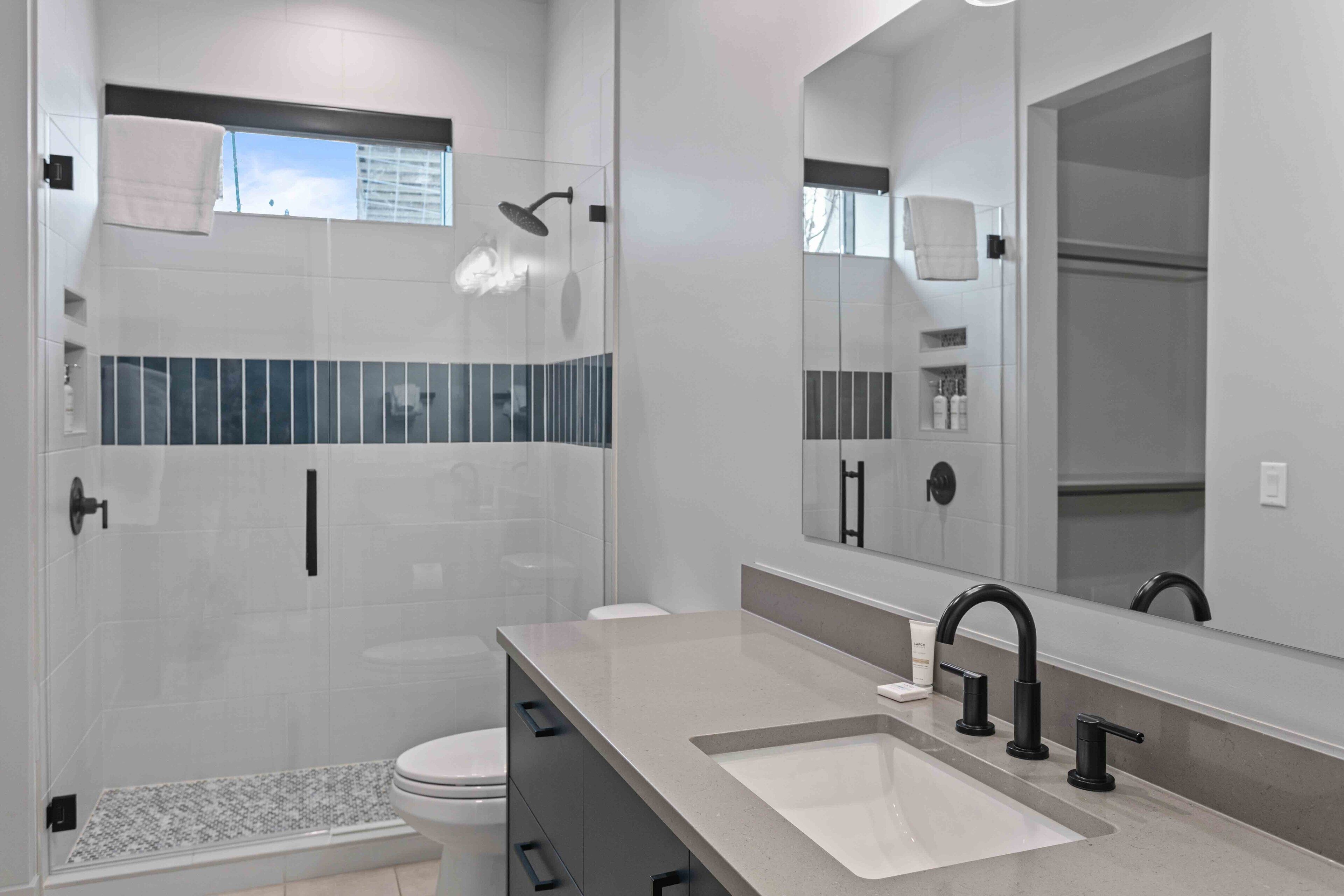 A modern bathroom with a glass-enclosed shower, a large mirror, and a countertop with a sink.