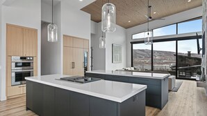 Une cuisine moderne dotée d’un grand îlot central, d’appareils électroménagers en acier inoxydable et de grandes fenêtres offrant une vue sur les montagnes.