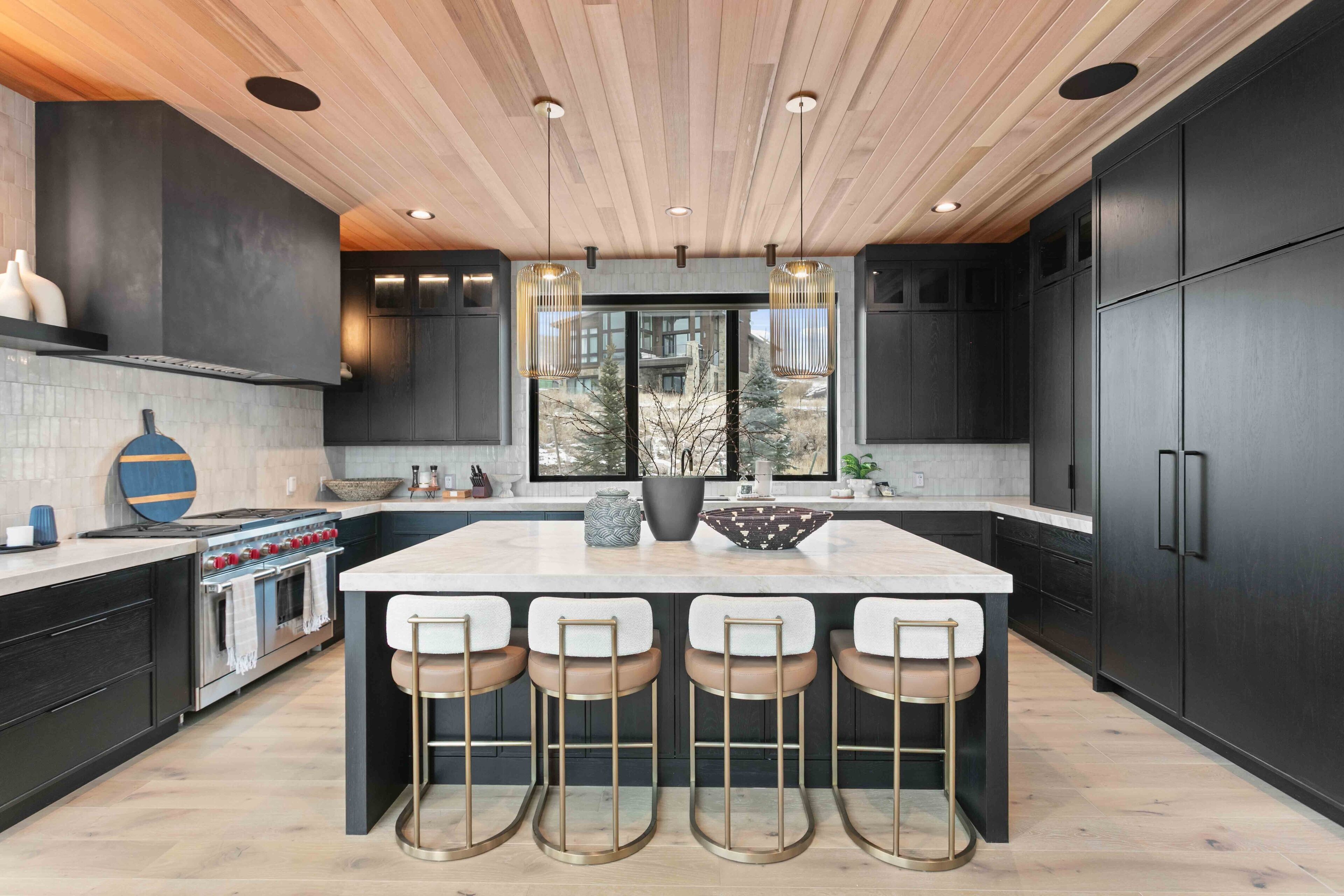 A modern kitchen with a large island, dark cabinetry, and a wooden ceiling.