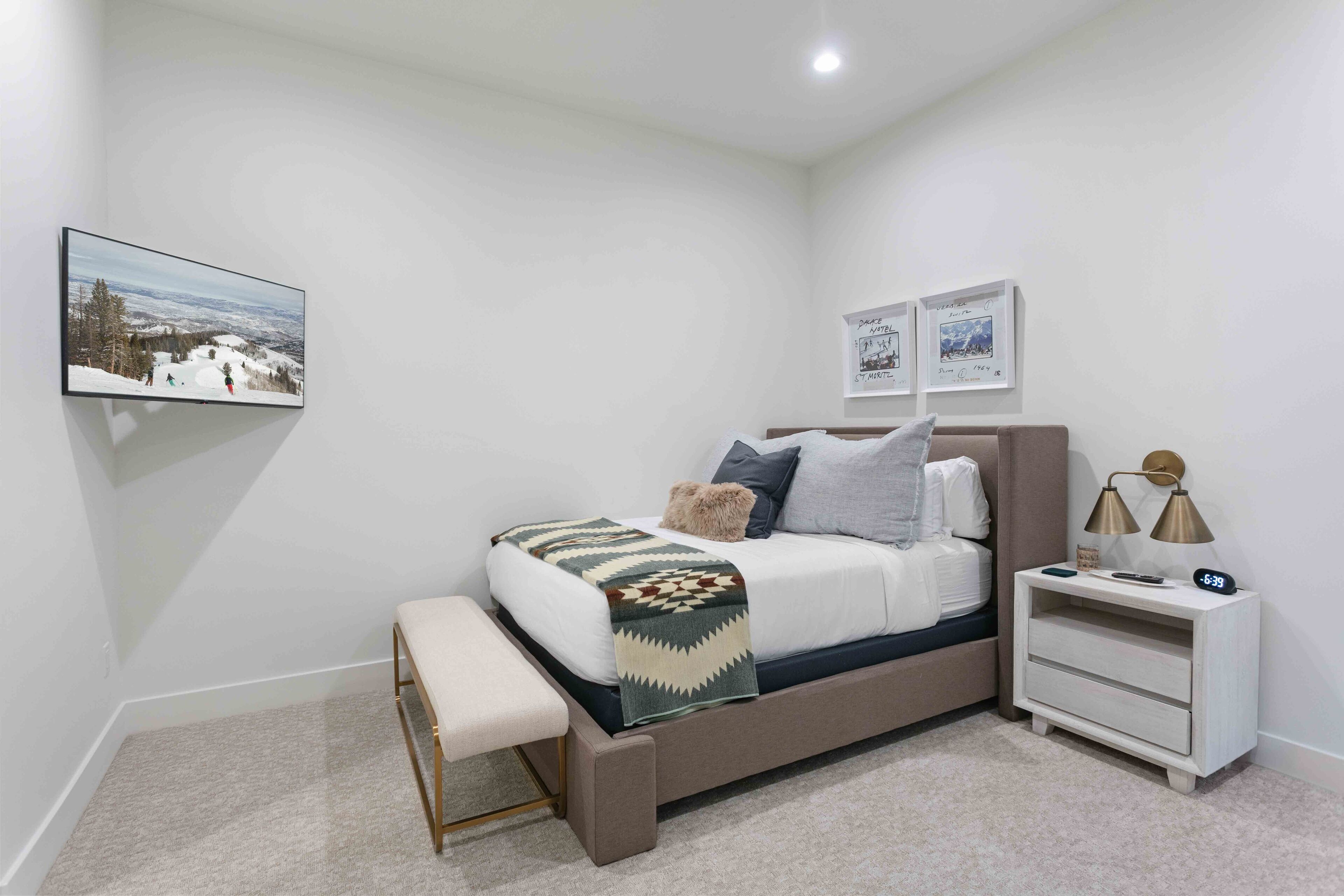 A bedroom with a bed, bedside tables, a bench, and wall art.