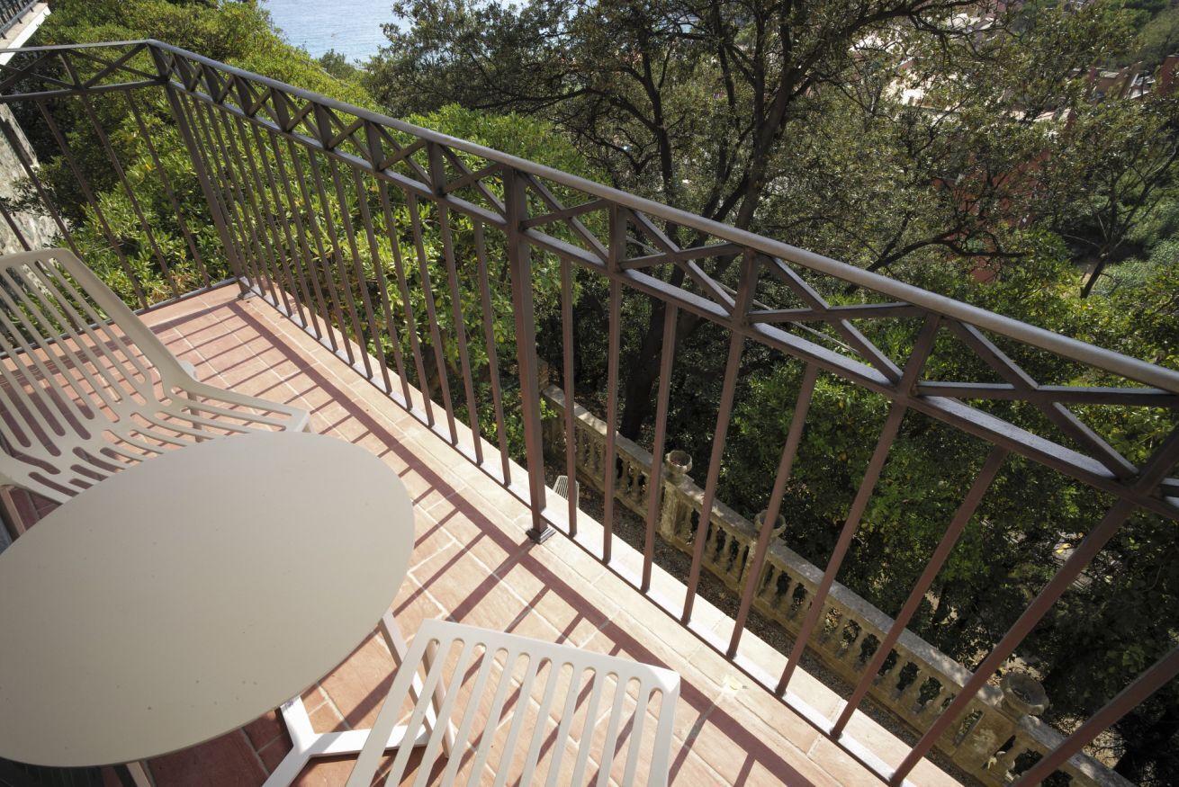 A balcony with a table and chairs, surrounded by a metal railing, overlooking a lush green area.