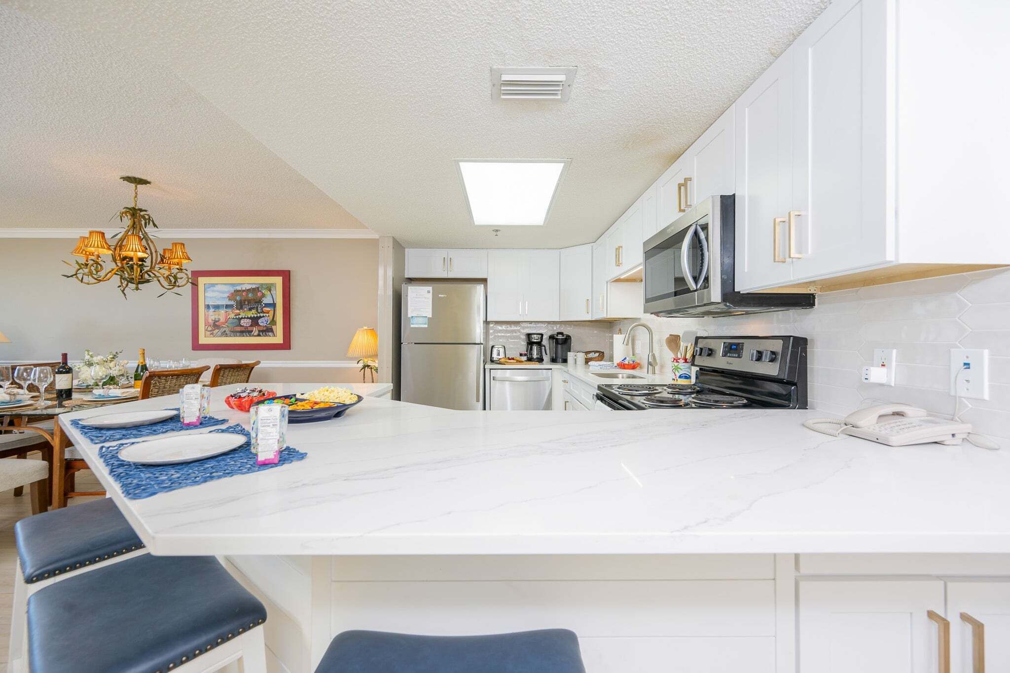 Une cuisine moderne avec des armoires blanches, un grand îlot central et un lustre.