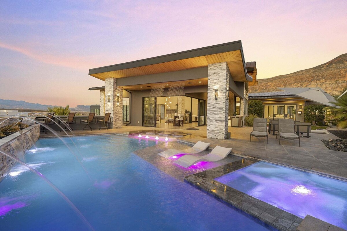 A modern outdoor pool area with a covered seating area, lounge chairs, and a view of the mountains.