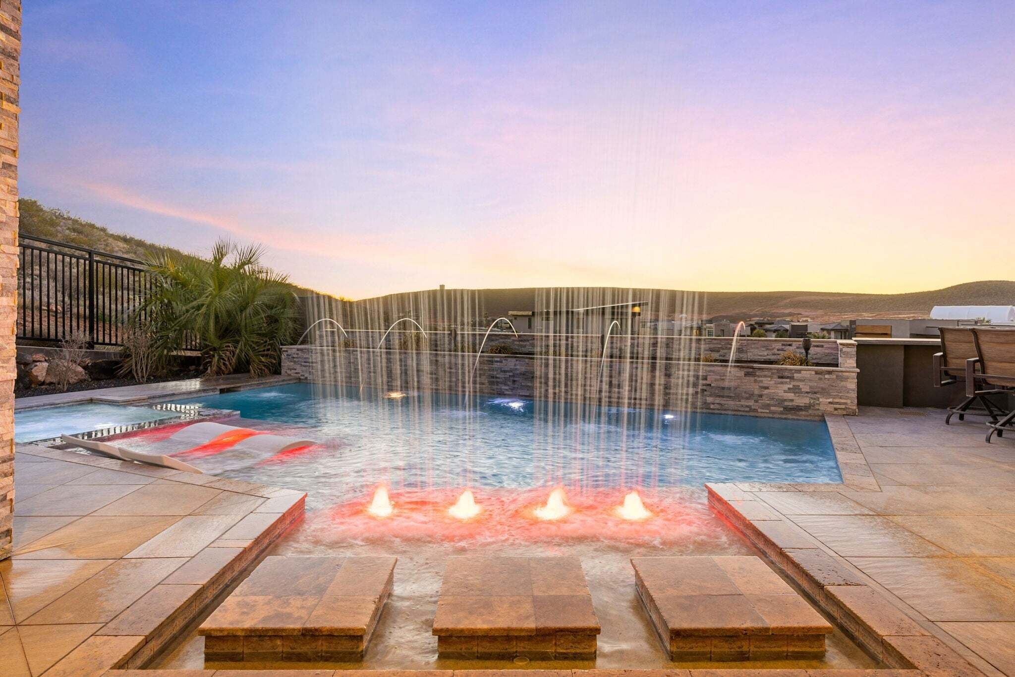 Ein Pool mit Wasserfall, umgeben von Steinmauern und einer Terrassenanlage.