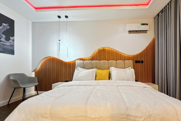 A modern bedroom with a wooden headboard, a bed with white bedding, a gray chair, and a wall-mounted air conditioner.
