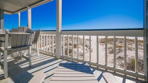 A covered outdoor area with a view of the beach, featuring a seating area with chairs and a table. - Regatta Condominiums 106b 3 Bedroom Condo (Gulf Shores)