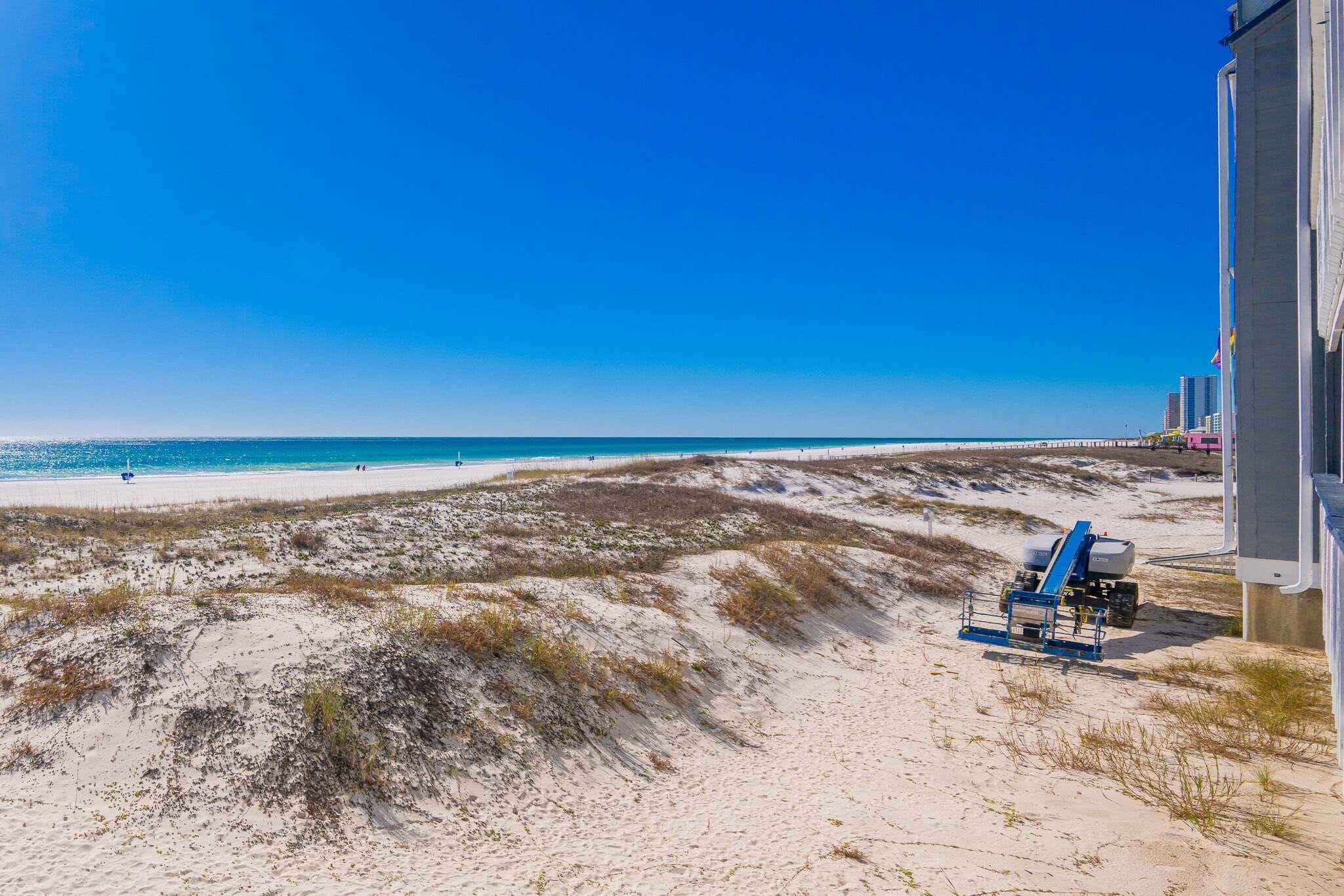 A beach with a dune system, a clear blue sky, and a distant pier.