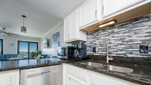 A modern kitchen with white cabinets, a granite countertop, a stainless steel sink, and a coffee maker. - Regatta Condominiums 106b 3 Bedroom Condo (Gulf Shores)