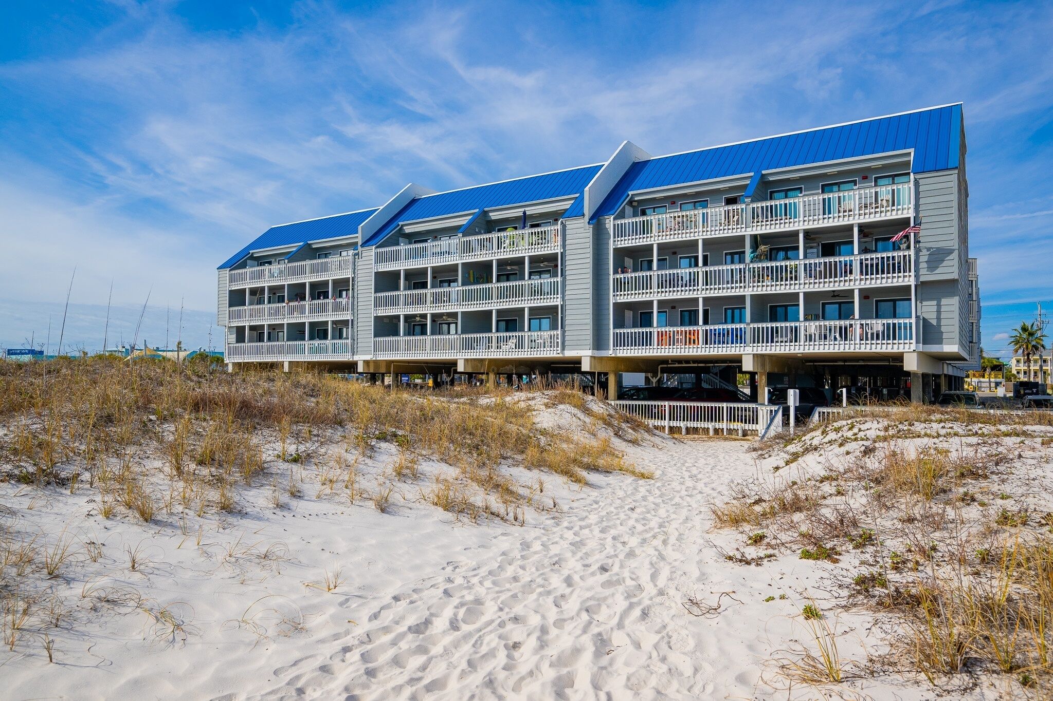 A beachfront hotel with multiple balconies, a sandy beach in front, and a clear sky.