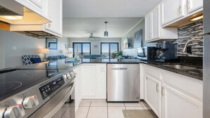 A modern kitchen with white cabinets, a stainless steel dishwasher, and a black countertop. - Regatta Condominiums 106b 3 Bedroom Condo (Gulf Shores)