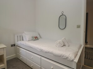 A small, single-bed room with a white bed, a small bedside table, and a wall-mounted mirror. - Two Hollens (Ambleside)